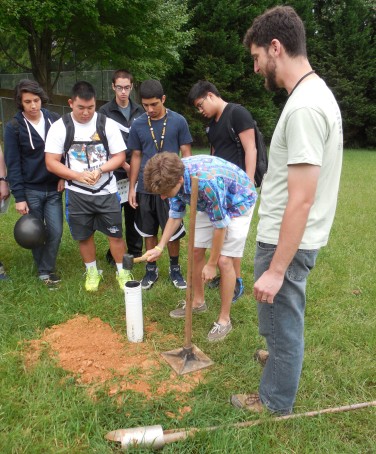 Student helps secure a pipe to perform a perk test.  Analysis of the perk test will enable students to evaluate the permeability of their campus soil
